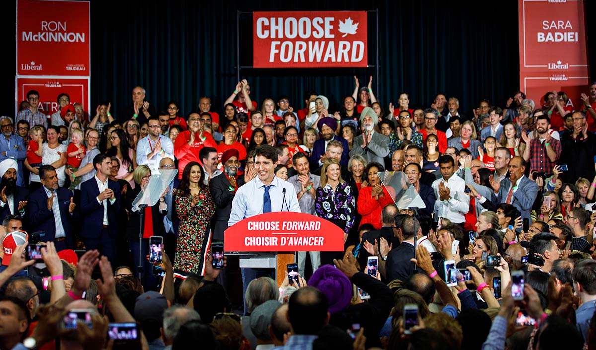 Justin Trudeau giving a speech at a podium, surrounded by hundreds of supporters