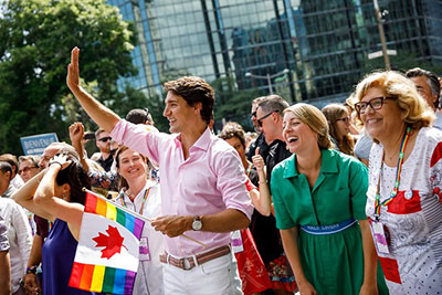 Justin Trudeau and Members of Parliament waving to the crowd at a Pride Parade.